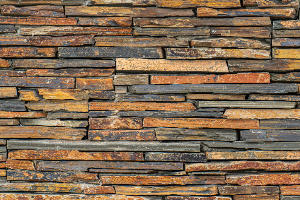 Panell de pedra natural Laja Multicolor amb peces allargades de disposició horitzontal, combinació d'ocres, marrons, grisos i negres, textura estriada i vetes marcades, per a façanes i revestiments amb caràcter — Construccions Ramilo