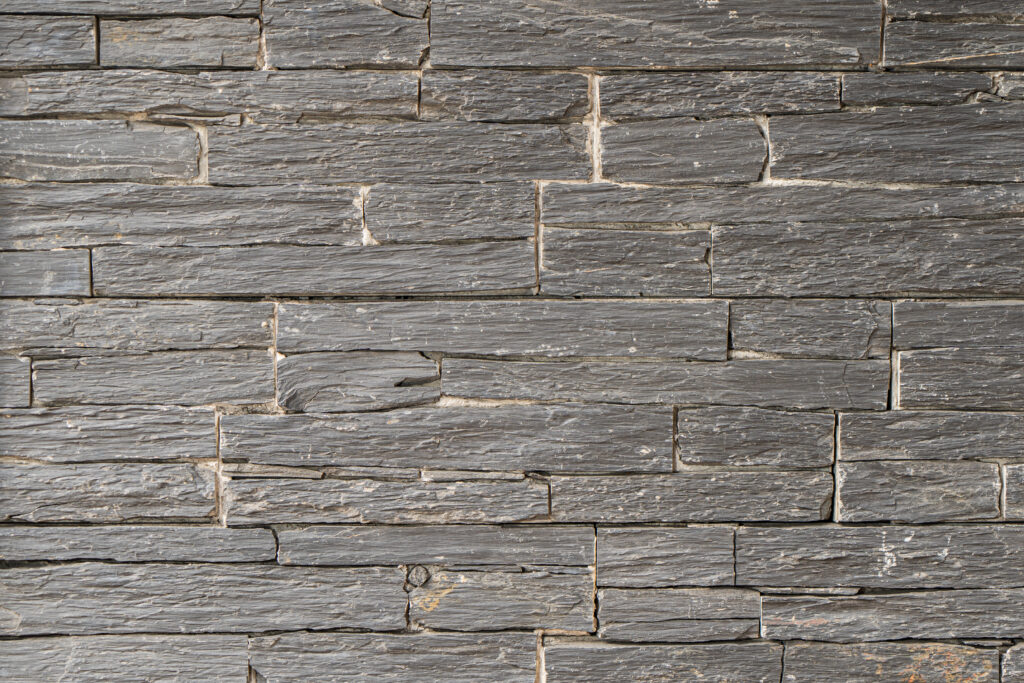 Panell de pedra natural Long Black amb peces molt allargades de disposició horitzontal, tonalitats negres i grisos foscos i textura estriada, per a façanes contemporànies sòbries — Construccions Ramilo