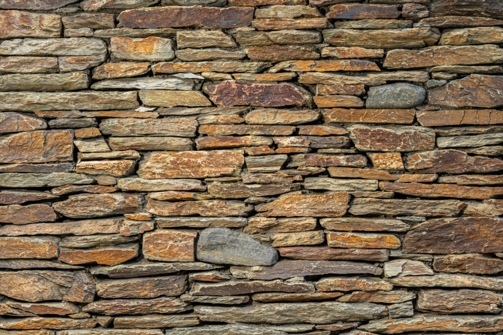 Mur de pedra artesana natural Barreja amb peces allargades de mides diverses, combinació de tons ocres, marrons i grisos terrosos, textura irregular i vetes marcades, per a murs amb personalitat i integració paisatgística — Construccions Ramilo