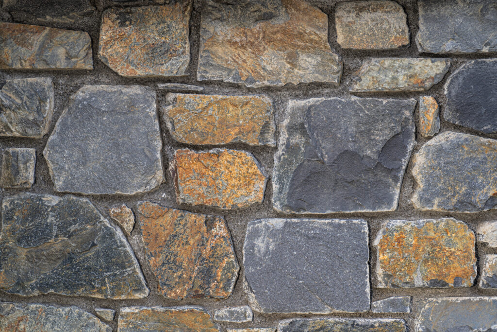 Mur de pedra artesana natural Pedra del País amb peces irregulars de mides i formes diverses, tons grisos amb matisos ocres i terrosos, textura marcada i vetes visibles, per a murs rústics amb forta connexió amb l'entorn — Construccions Ramilo