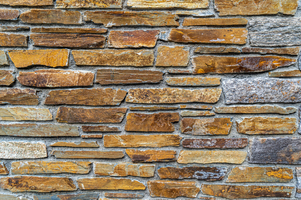 Mur de pedra artesana natural Taco L amb peces estretes i allargades de disposició horitzontal, tons ocres, marrons i beix, textura estriada i vetes visibles, per a murs rústics amb caràcter — Construccions Ramilo
